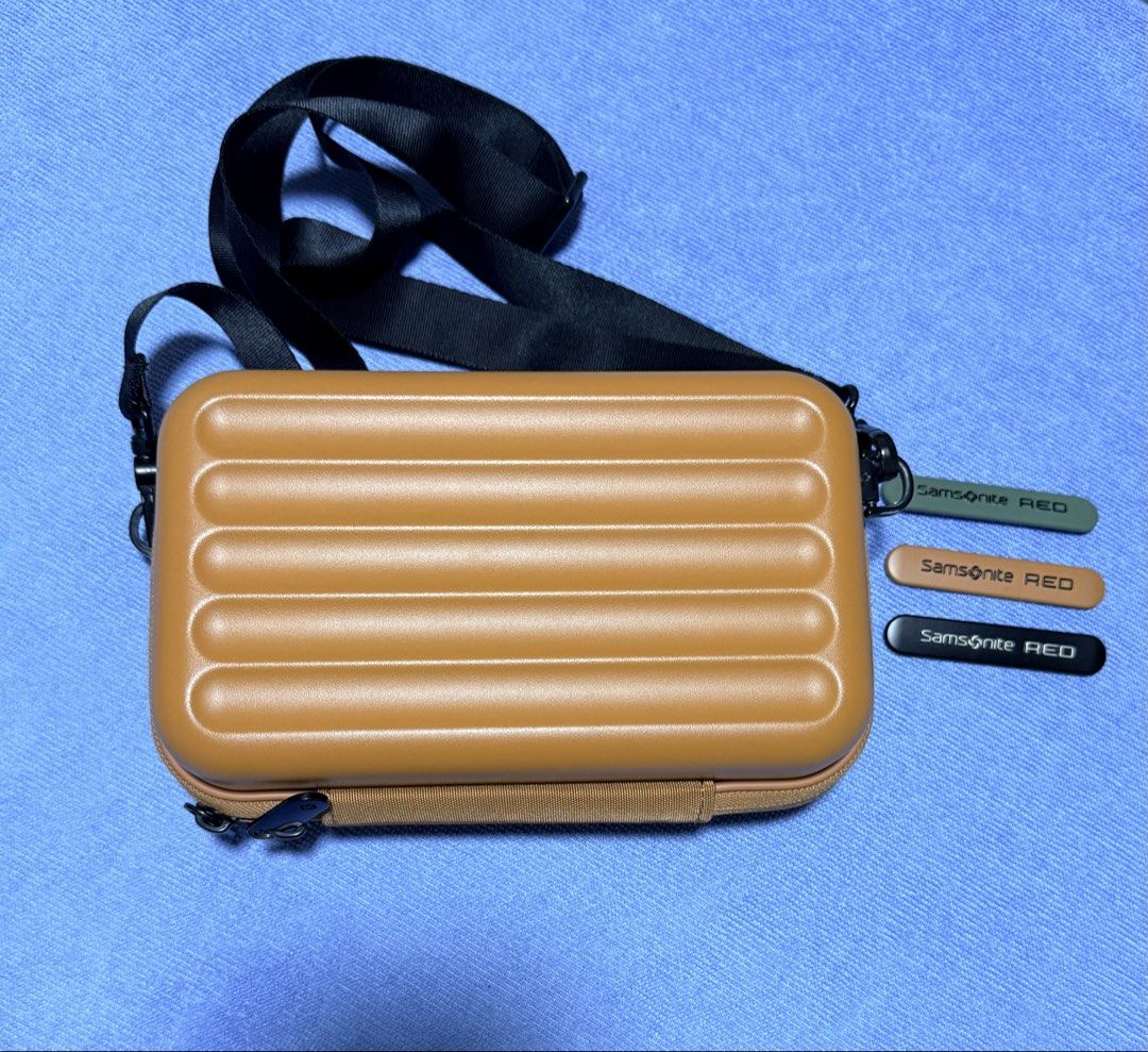 Samsonite RED hard shell crossbody bag tan (Category: Cross-body Bags) located in Dasmarinas. Submitted by toyang50 (Listing ID 1466780567, Image 2). Description: Samsonite RED hard shell crossbody bag in a tan colorway. Ridged hard exterior design paired with a red logo badge. Adjustable black shoulder strap included. Interior lined with yellow fabric, featuring mesh pockets and compartments for organization. Three interchangeable color tags in 