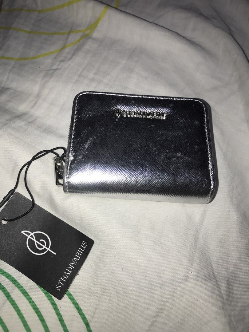 Stradivarius Metallic Silver Zip Around Wallet (Category: Wallets & Card holders) located in Pasig City. Submitted by papotzy (Listing ID 1466911615, Image 1). Description: Stradivarius zip around wallet in a metallic silver finish. Compact size with multiple card slots and zipped coin compartments inside. Structured design with textured material exterior. Original tag attached with price marked in PHP. Never used, tag still hanging on the zipper