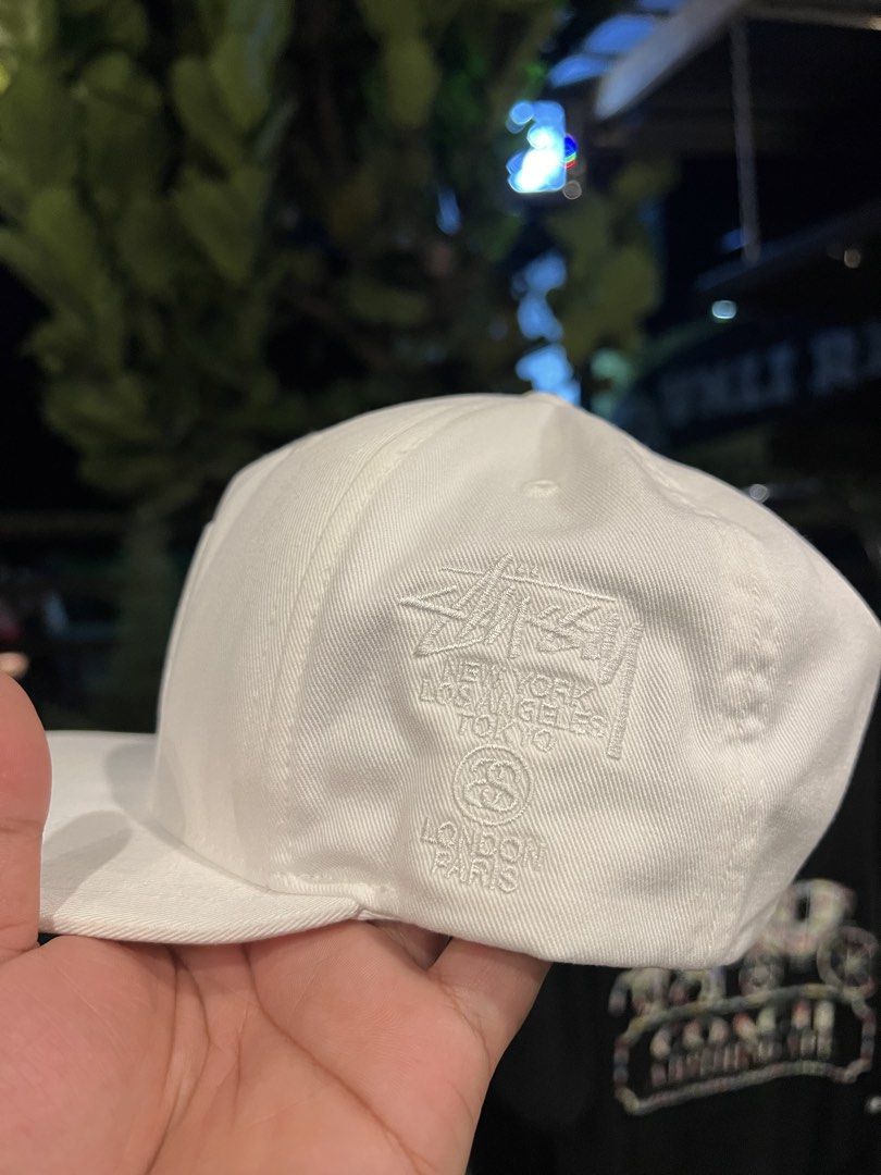 Stüssy White Snapback Hat Cap (Category: Caps & Hats) located in Manila. Submitted by wearurlux_wul (Listing ID 1466808267, Image 2). Description: - Brand: Stüssy - Color: White - Style: Snapback hat / Cap - Fit: Standard OS (One Size, Adjustable) - Material: 100% Cotton - Design: Stitched round logo on front, embroidered global cities (NYC, LA, Tokyo, London, Paris) on the side - Closure: Adjustable plastic snap with small woven logo tab - Condi