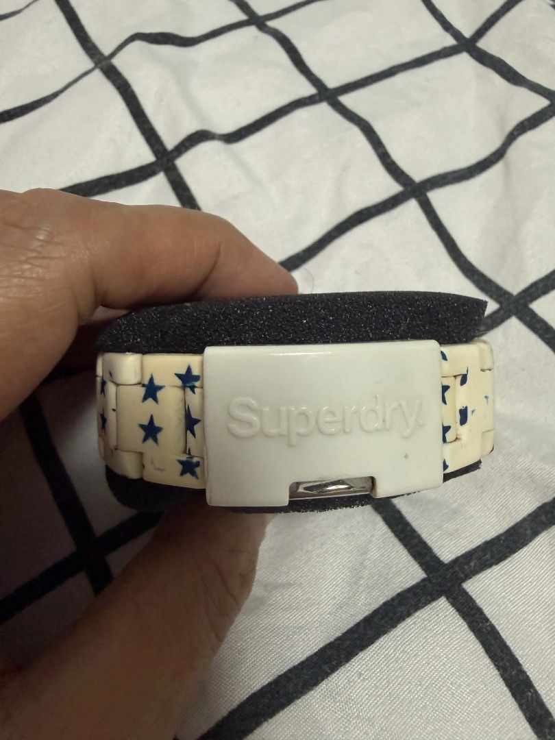 Superdry Japan Movement (Category: Women's Watches) located in Hermosa. Submitted by marywilma (Listing ID 1466864417, Image 2). Description: Superdry watch with white and blue star pattern strap. Blue bezel framing a white dial featuring bold numbers. Japan movement with 10 ATM water resistance. White deployment clasp stamped with Superdry logo. Stainless steel case back. Shows minor discoloration on the white strap links..