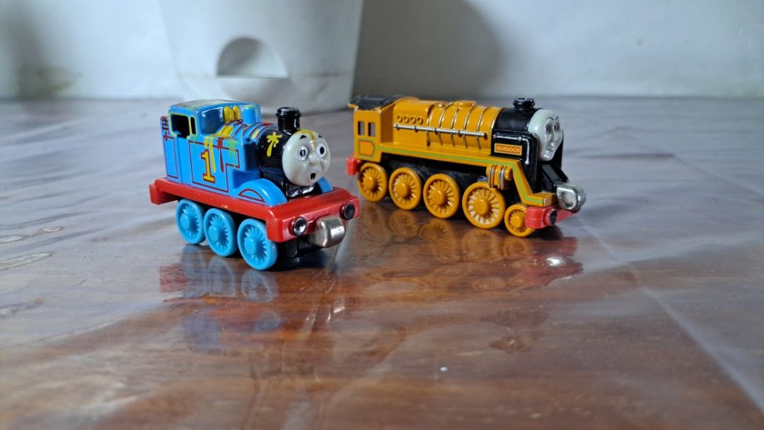 Thomas train (Category: Kids Toys) located in Quezon City. Submitted by hersheejubilo (Listing ID 1466904450, Image 2). Description: - Set includes 2 Thomas & Friends characters: Thomas (blue No. 1) and Murdoch (yellow engine) - Durable die-cast metal construction with rolling wheels - Equipped with magnetic couplers to link the trains together - Fun paint-splatter design details on Thomas - Layered condition 4/10, showing visible wear from play 
