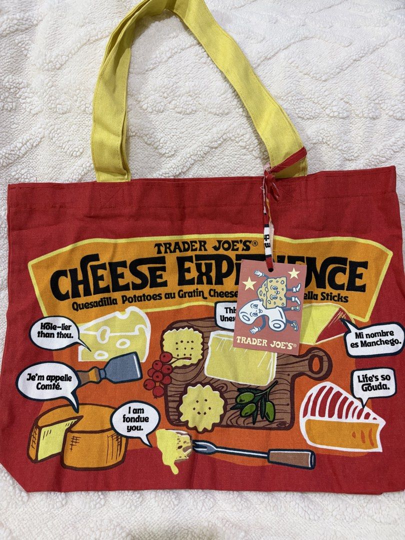 Trader Joe's Cheese Experience Tote Bag (Category: Tote Bags) located in Paranaque City. Submitted by greatfinds108 (Listing ID 1466862868, Image 1). Description: - Authentic Trader Joe's canvas tote bag - Vibrant red body with sturdy yellow handles - Fun cheese and cracker graphic print with funny puns - Brand new with original tag attached - Roomy interior, perfect for grocery shopping or casual everyday use - Clean surface with bright, lasting
