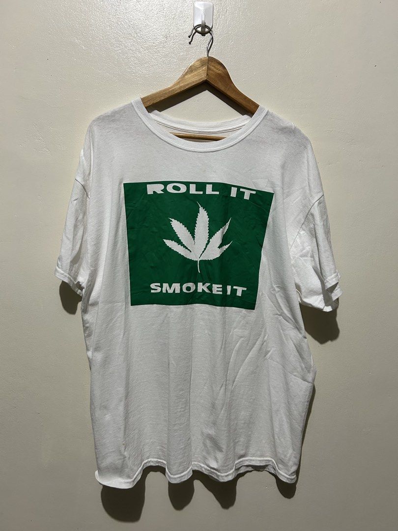 White Roll It Smoke It Graphic Tee (Category: Tshirts & Polo Shirts ) located in Angeles City. Submitted by johngamboa (Listing ID 1466962203, Image 1). Description: - Color: White - Style: Short sleeve crew neck t-shirt with relaxed fit - Design: Bold green 'ROLL IT / SMOKE IT' box graphic with white cannabis leaf - Material: Soft cotton - Condition: Pre-loved with normal signs of wear.