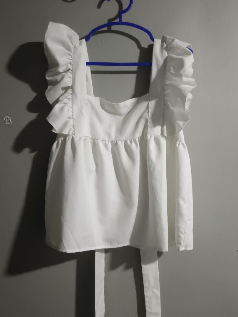 White Ruffle Strap Tie Back Peplum Top (Category: Sleeveless) located in Trece Martires City. Submitted by fleurdelis.67 (Listing ID 1466904422, Image 1). Description: - Color: Solid white - Style: Sleeveless peplum top with square neckline - Details: Dramatic ruffle straps & adjustable long back ties - Fit: Gathered empire waist for a flattering, flowy shape - Fabric: Lightweight and breathable, ideal for sunny days - Condition: Excellent / Bran