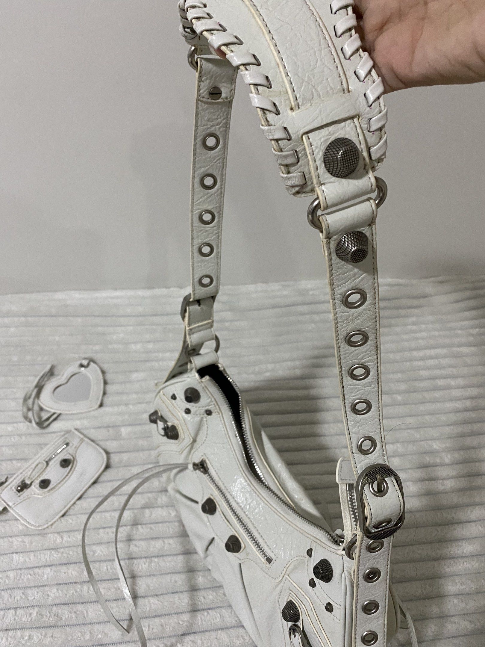 Balenciaga Le Cagole Shoulder Bag (Category: Luxury Bags & Wallets) located in Santa Rosa. Submitted by sassycollection. (Listing ID 1419153976, Image 2). Description: White Balenciaga Le Cagole shoulder bag. Features a curved shape, studded details, and a detachable heart-shaped mirror. Includes a detachable coin purse. The bag has a zip closure and an adjustable shoulder strap. The interior is black. The exterior has a textured finish..