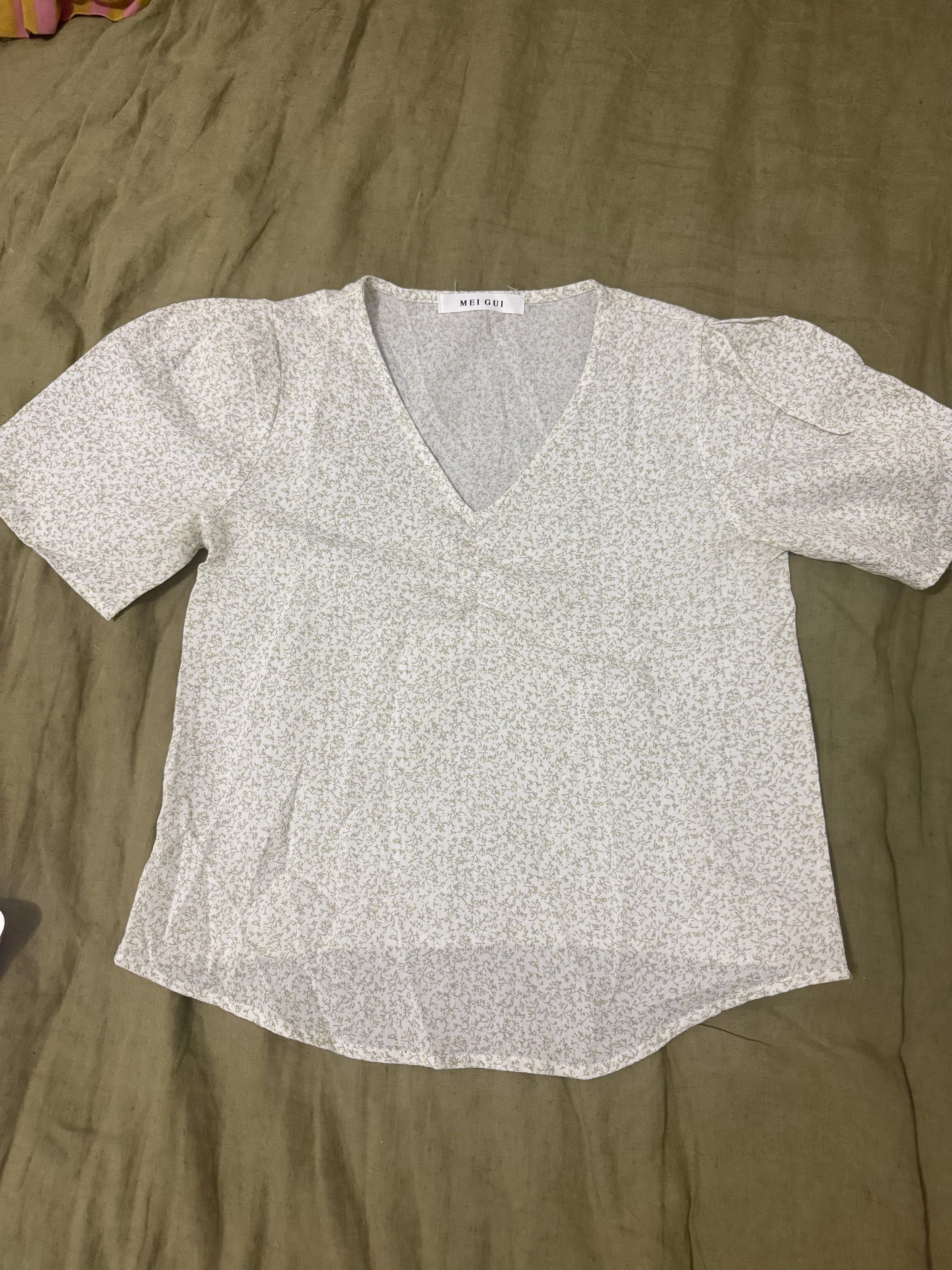 MEI GUI Floral V-Neck Blouse (Category: Blouses) located in Paranaque City. Submitted by bailey_cade (Listing ID 1419133506, Image 1). Description: Floral blouse with a V-neck design. Features short sleeves and a slightly puffed shoulder. The blouse has a delicate floral pattern in shades of white and green. The brand tag is visible. Measurements are provided in the images. Used so please manage your expectations .