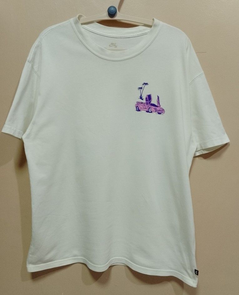 Nike SB Graphic Tee (Category: Tshirts & Polo Shirts ) located in Antipolo. Submitted by technothrift (Listing ID 1420768459, Image 2). Description: - White Nike SB t-shirt - Graphic print on front and back - Back graphic: City scene with car and figure - Front graphic: Car and palm trees - Crew neck - Short sleeves - Minor stains.