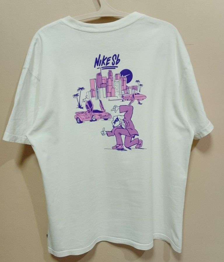 Nike SB Graphic Tee (Category: Tshirts & Polo Shirts ) located in Antipolo. Submitted by technothrift (Listing ID 1420768459, Image 1). Description: - White Nike SB t-shirt - Graphic print on front and back - Back graphic: City scene with car and figure - Front graphic: Car and palm trees - Crew neck - Short sleeves - Minor stains.