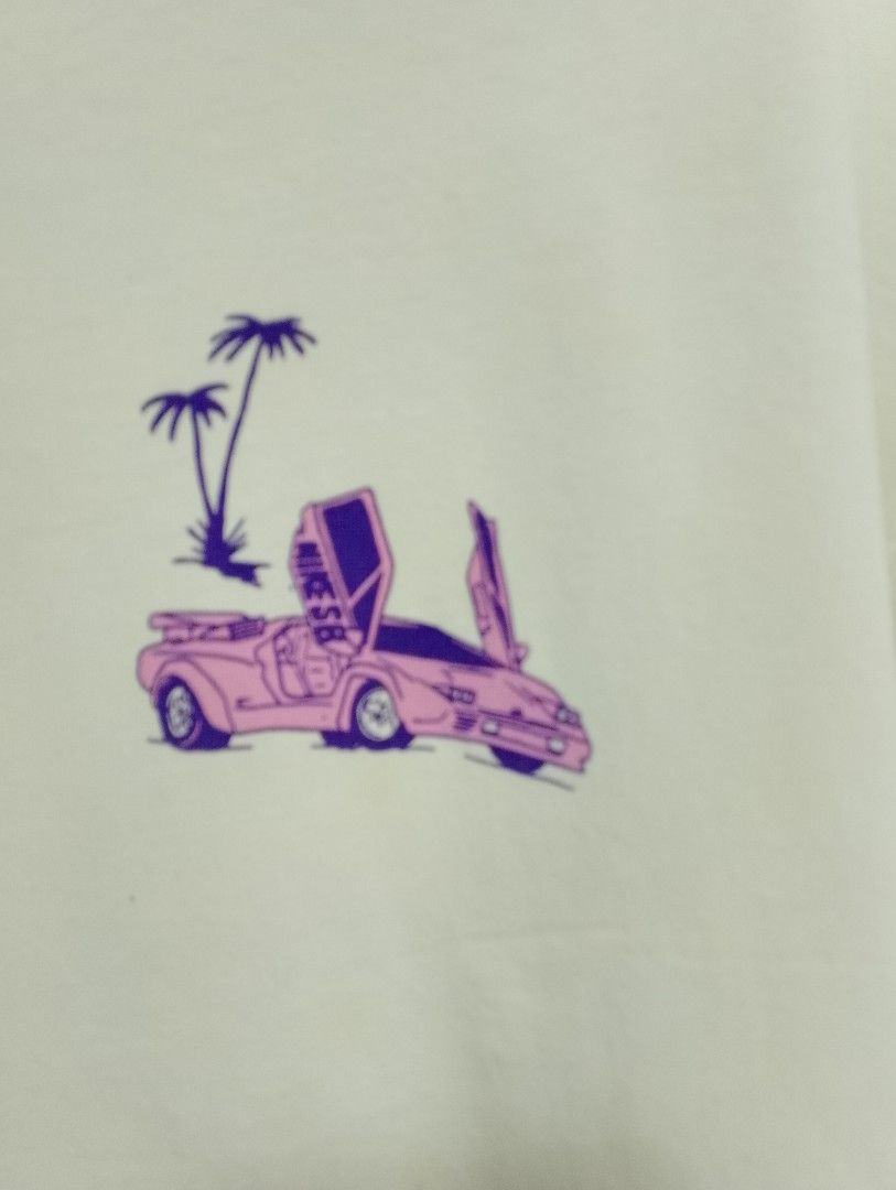 Nike SB Graphic Tee (Category: Tshirts & Polo Shirts ) located in Antipolo. Submitted by technothrift (Listing ID 1420768459, Image 3). Description: - White Nike SB t-shirt - Graphic print on front and back - Back graphic: City scene with car and figure - Front graphic: Car and palm trees - Crew neck - Short sleeves - Minor stains.