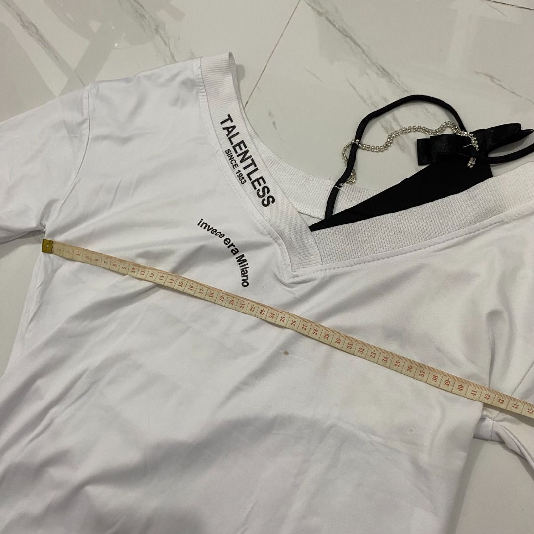 Talentless White V-Neck T-Shirt (Category: Others Tops) located in San Fernando. Submitted by deku_off (Listing ID 1420888651, Image 2). Description: White Talentless T-shirt with a V-neck design. Features the text "TALENTLESS SINCE 1953" and "invece era Milano" printed on the neckline. Includes a black strap with a chain and a tag. The shirt has short sleeves. Note: with tiny stain.