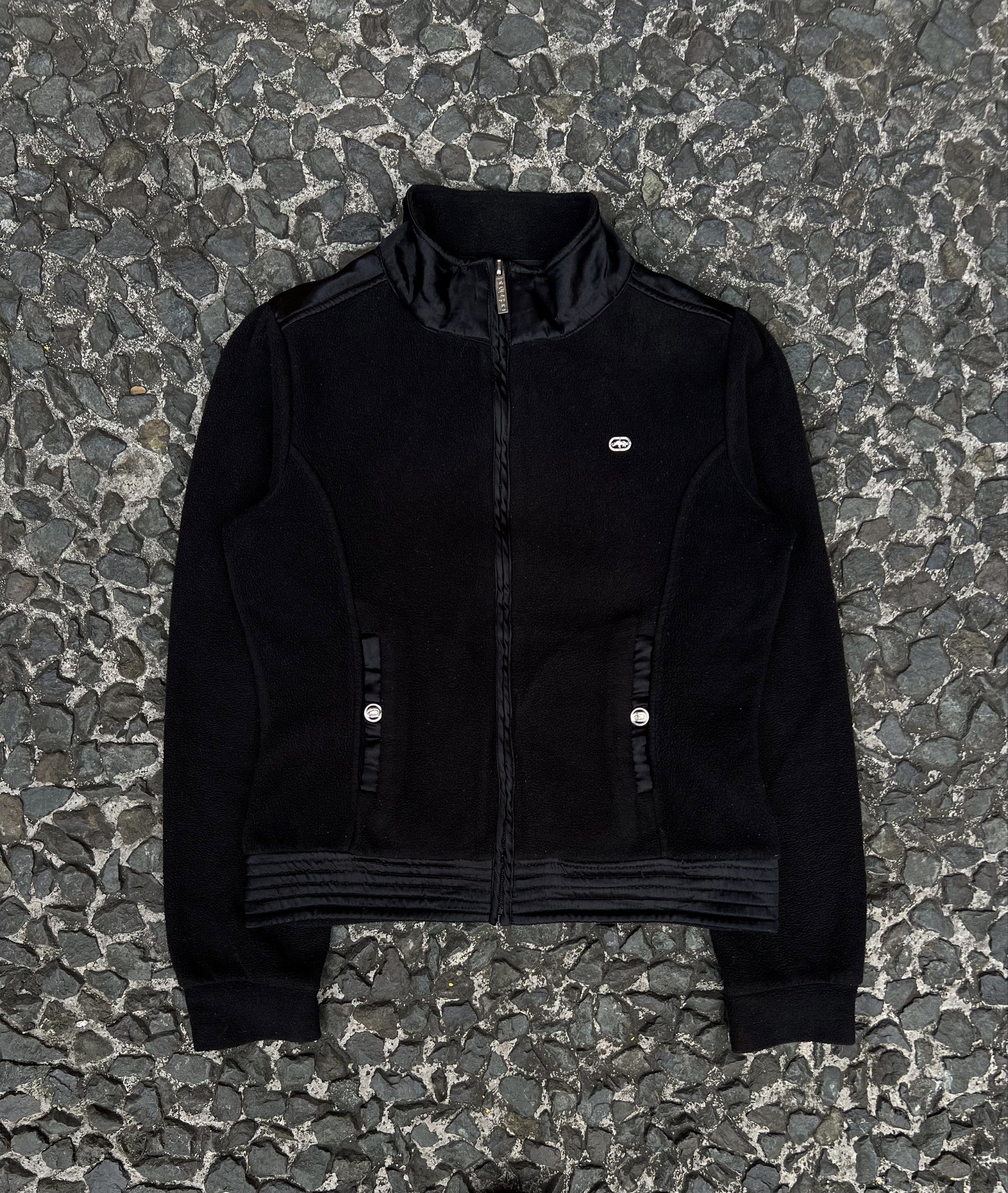 Ecko Unltd. Womens Y2k Black Fleece Jacket (Category: Coats, Jackets and Outerwear) located in Quezon City. Submitted by shanks. (Listing ID 1421040752, Image 1). Description: Black fleece jacket from Ecko Unltd. Features a full zip closure, a high collar, and the Ecko Unltd. logo on the chest and back. The jacket has two pockets with button details. Size : Medium Dimensions : Length: 22 Width: 19 Shoulder : 14 Sleeve : 25 Sign of used .