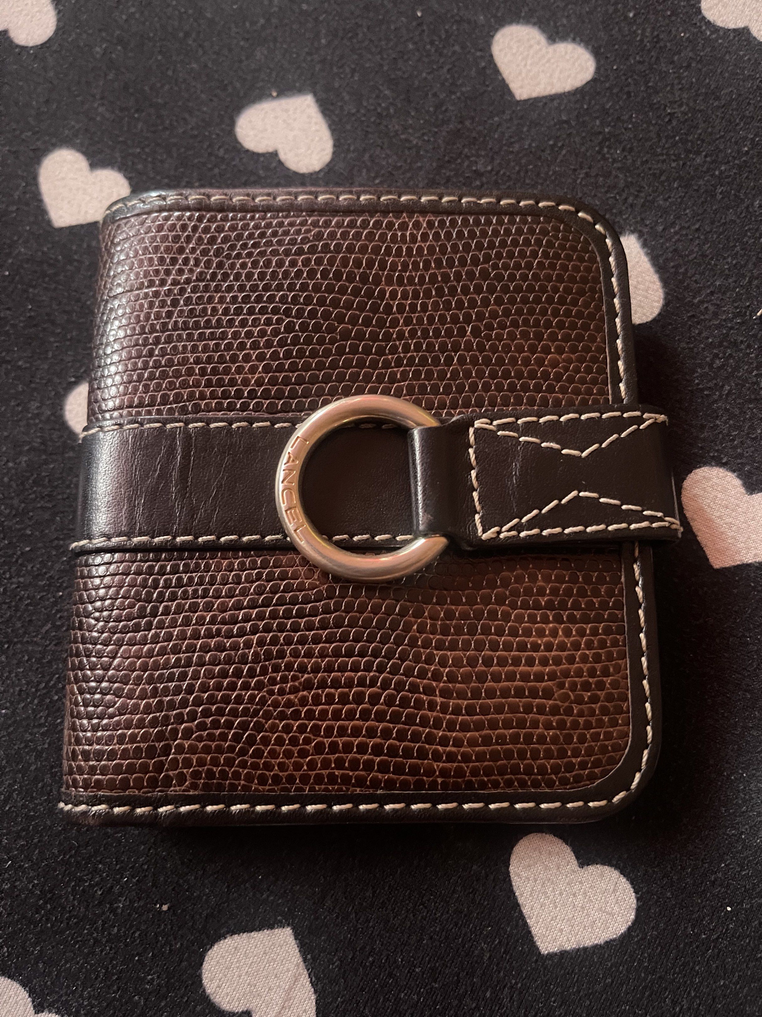 Lancel Short Wallet (Category: Luxury Bags & Wallets) located in Quezon City. Submitted by minekoh21 (Listing ID 1421016441, Image 1). Description: - Authentic Lancel Paris Luxury wallet - Genuine leather wallet - Textured exterior - Dark brown leather strap - Silver-tone ring closure with Lancel branding - Multiple card slots - Coin pocket - Bill compartment - White stitching - Patterned lining RFS: Decluttering.