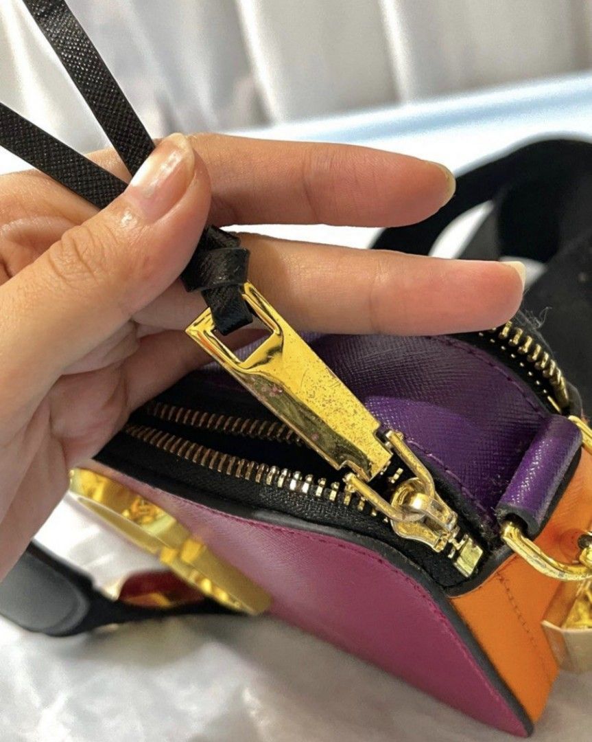 Marc Jacobs Bag (Category: Luxury Bags & Wallets) located in Bacoor. Submitted by nd.clothing (Listing ID 1420978929, Image 2). Description: Marc Jacobs The Box Bag features a vibrant color block design with a gold-tone logo. It has a detachable strap with gold hardware and studded details. The bag has a zip closure and multiple compartments. The interior is lined with purple material. The bag has a black strap and gold hardware..