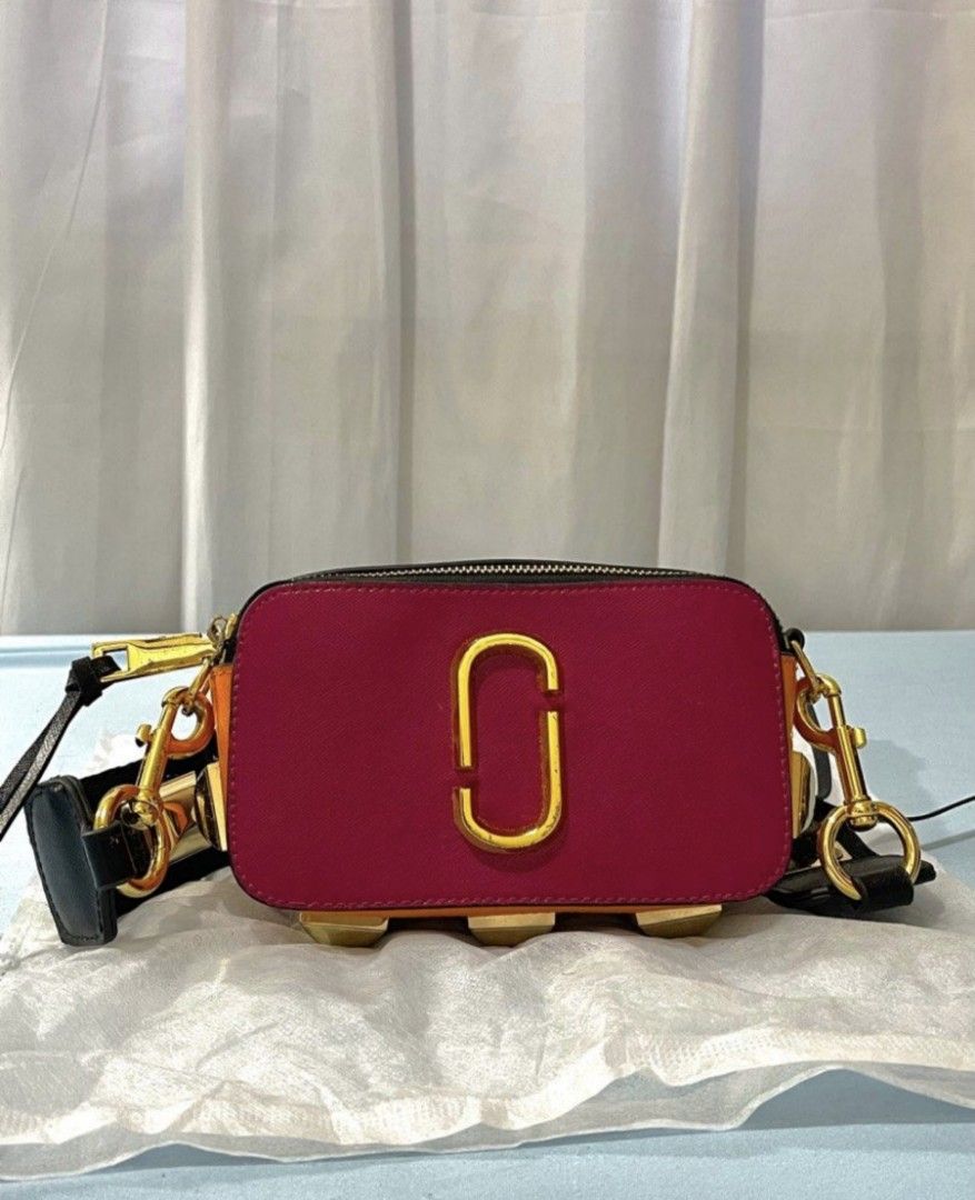 Marc Jacobs Bag (Category: Luxury Bags & Wallets) located in Bacoor. Submitted by nd.clothing (Listing ID 1420978929, Image 1). Description: Marc Jacobs The Box Bag features a vibrant color block design with a gold-tone logo. It has a detachable strap with gold hardware and studded details. The bag has a zip closure and multiple compartments. The interior is lined with purple material. The bag has a black strap and gold hardware..