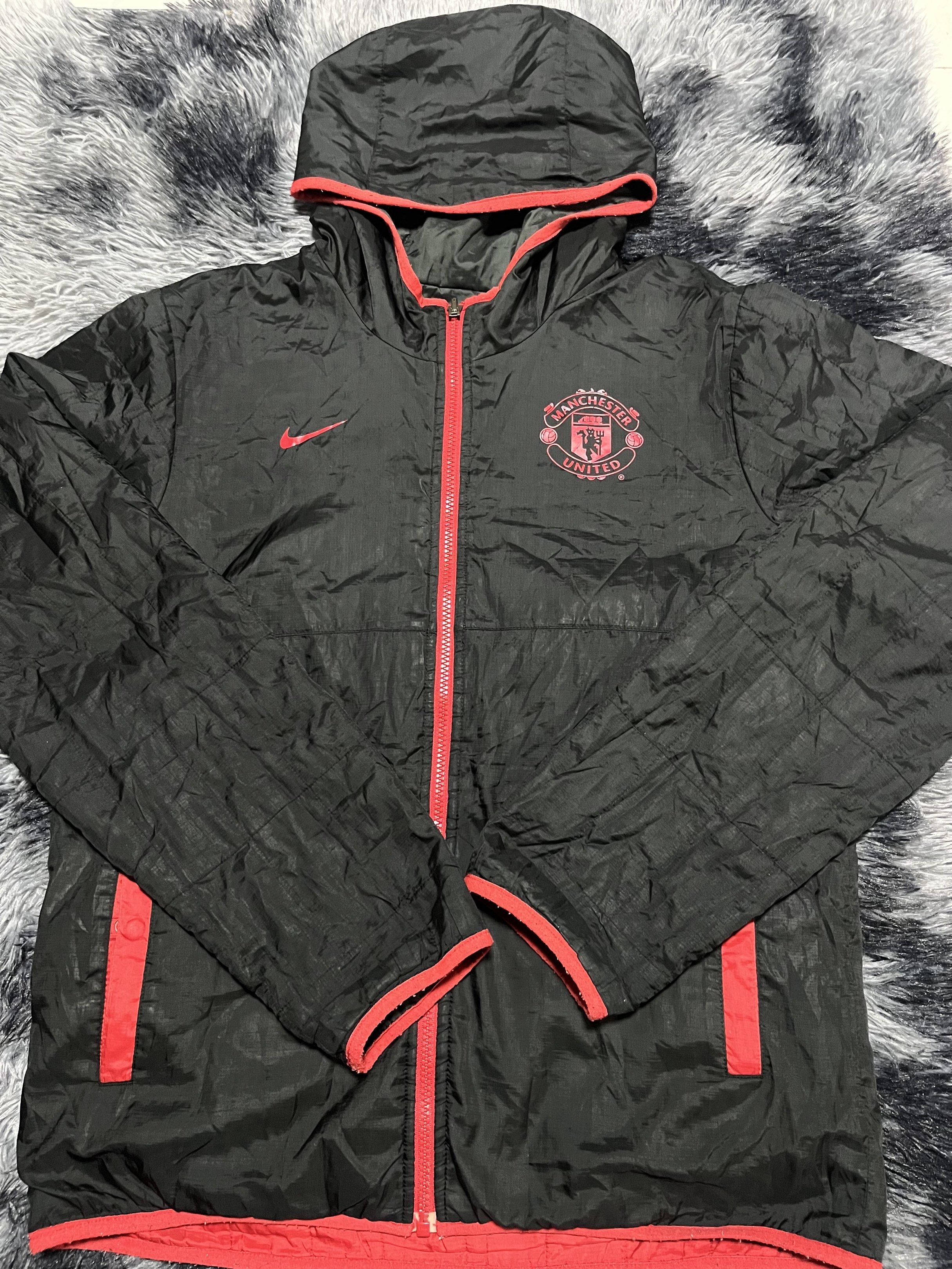 Nike Manchester United Reversible Jacket (Category: Coats, Jackets and Outerwear) located in Santa Rosa. Submitted by _unclethrifts (Listing ID 1421096235, Image 1). Description: - Reversible Manchester United jacket. - One side: Black with red accents. - Other side: Red with black accents. - Includes a hood. - Full-length zipper. - Nike logo on the chest. - Size tag present..