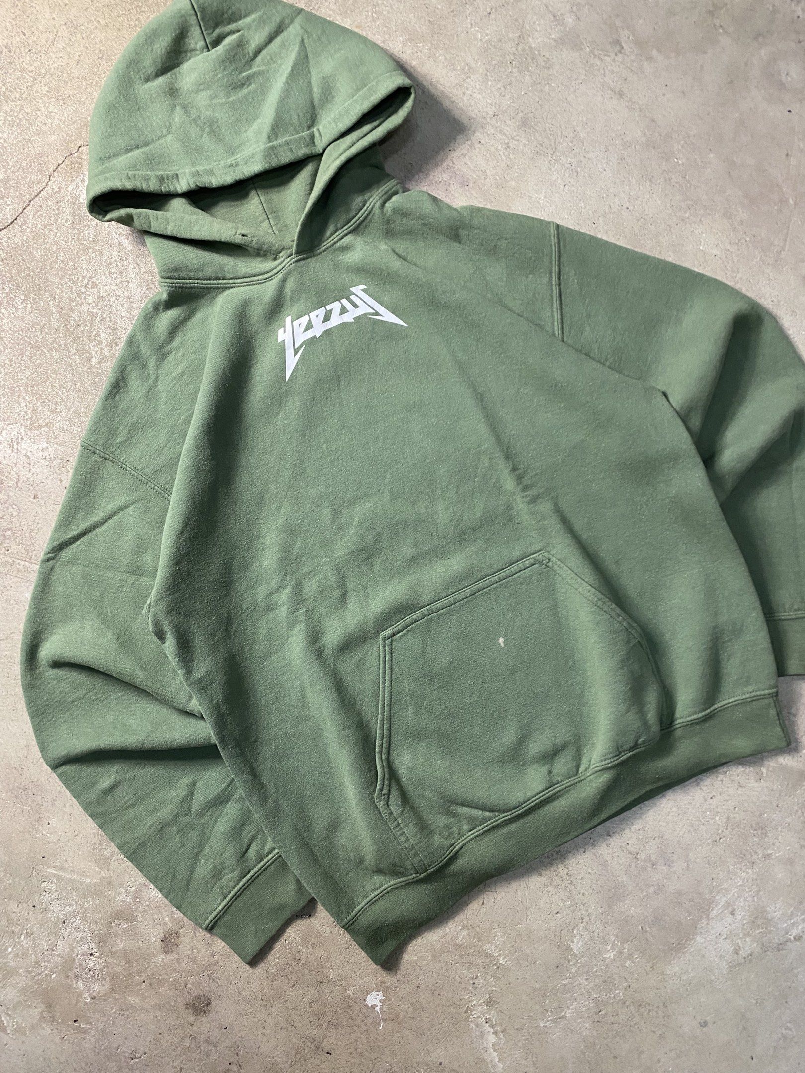 Yeezy Hoodie Olive Green (Category: Hoodies) located in Angeles City. Submitted by driptee_ph22 (Listing ID 1420938505, Image 2). Description: YEEZUS HOODIE - Width:22 - Length:28 - Olive green Yeezy hoodie - Features a "Yeezy" graphic on the back - Relaxed fit - Made of thick cotton material - Has a front pocket and hood - Minor stains on the sleeve.