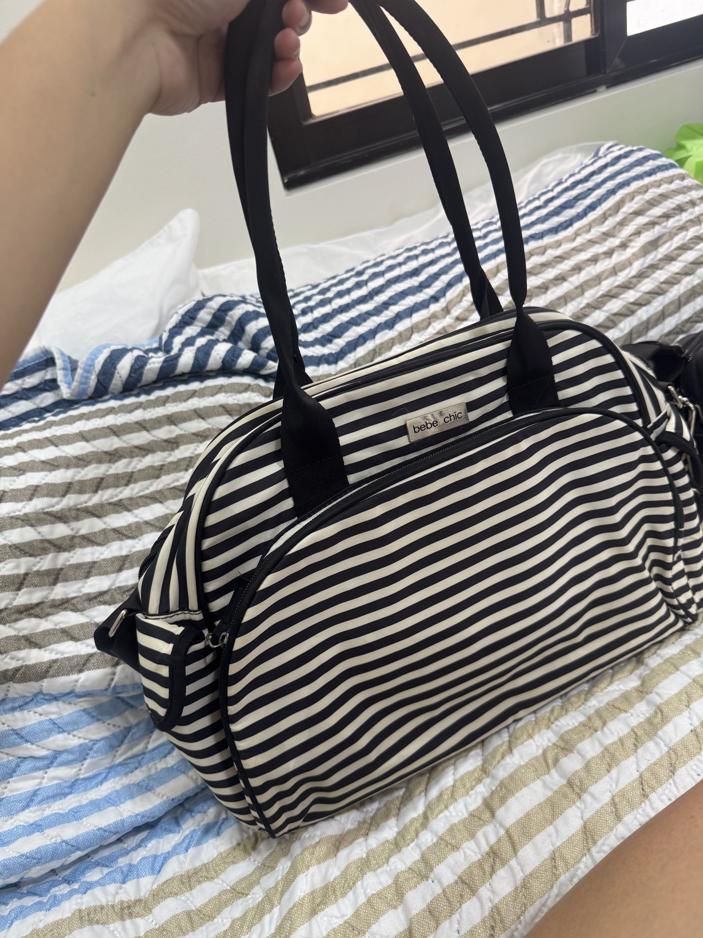 Bebe Chic Striped Diaper Bag (Category: Diaper Bags & Wetbags) located in Las Pinas. Submitted by babyandmommapreloved (Listing ID 1421150991, Image 1). Description: Stylish Bebe Chic diaper bag with a black and white striped design. Features multiple compartments and pockets for organization. Includes a changing mat. Comes with both hand straps and a shoulder strap for versatile carrying options. The interior shows some signs of use. Stains can 