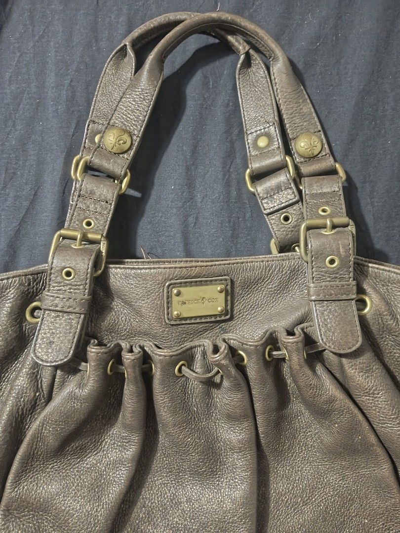 Patrick Cox Brown Leather Handbag | city bag (Category: Luxury Bags & Wallets) located in Makati City. Submitted by elirei (Listing ID 1421266658, Image 2). Description: - Patrick Cox brown leather handbag - Drawstring closure - Adjustable straps with buckle details - Interior zippered pocket with brand logo - Textured leather exterior - Dark fabric lining - Multiple compartments -Thick leather -Quite heavy Has sign of usage, ends rubs negotiatia