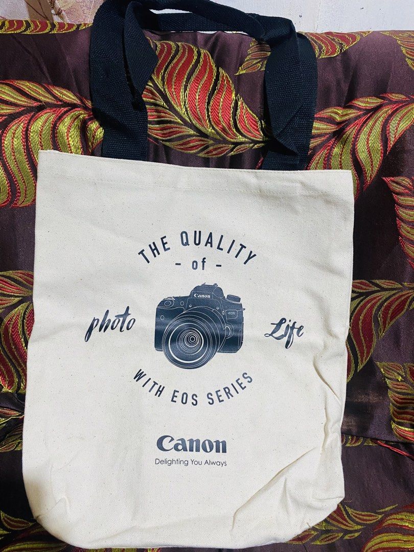 Canon Tote Bag (Category: Tote Bags) located in Baguio. Submitted by vanity_kimo (Listing ID 1421386226, Image 2). Description: ‼️SOLD AS SET ‼️ - Two Canon tote bags - Bag 1: "The Quality of Photo with EOS Series" and Canon logo - Bag 2: "Imagination Can You Imagine" - Cream-colored canvas material - Available with black or red straps .