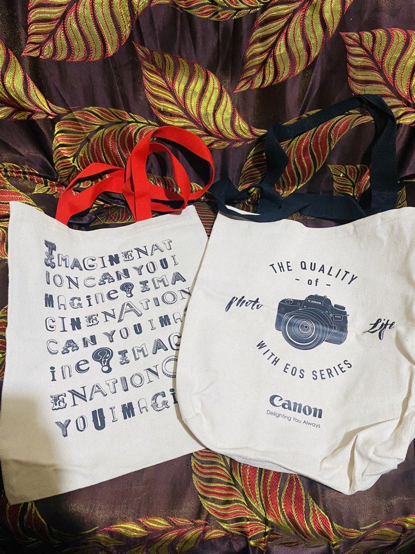Canon Tote Bag (Category: Tote Bags) located in Baguio. Submitted by vanity_kimo (Listing ID 1421386226, Image 1). Description: ‼️SOLD AS SET ‼️ - Two Canon tote bags - Bag 1: "The Quality of Photo with EOS Series" and Canon logo - Bag 2: "Imagination Can You Imagine" - Cream-colored canvas material - Available with black or red straps .
