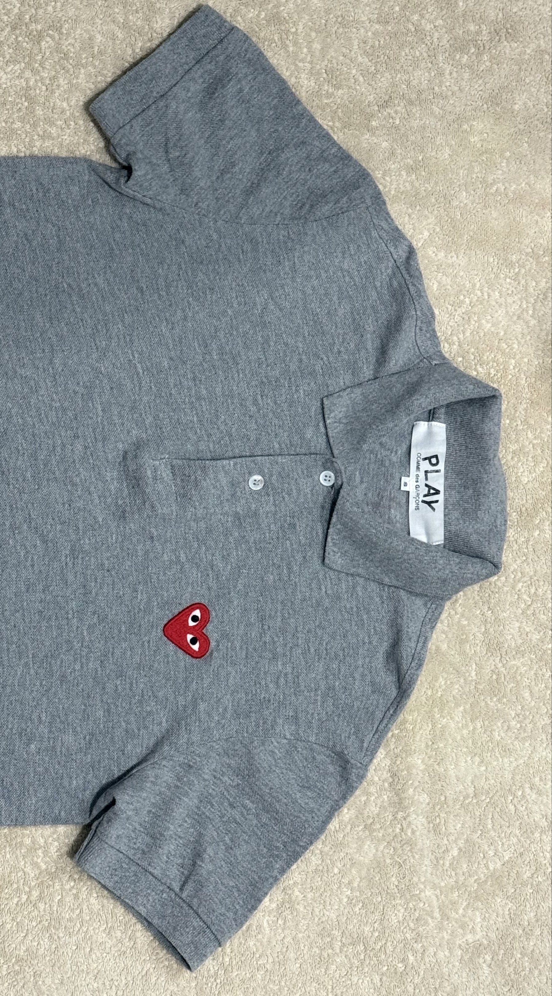 Comme des Garcons Play Polo Shirt (Category: Tshirts & Polo Shirts ) located in Manila. Submitted by jpadapat21 (Listing ID 1421403214, Image 2). Description: Authentic - Comme des Garcons Play polo shirt - Gray color - Features the iconic heart logo - Collared neckline - Button closure - Short sleeves - Classic fit - Size tag visible - 18x26.