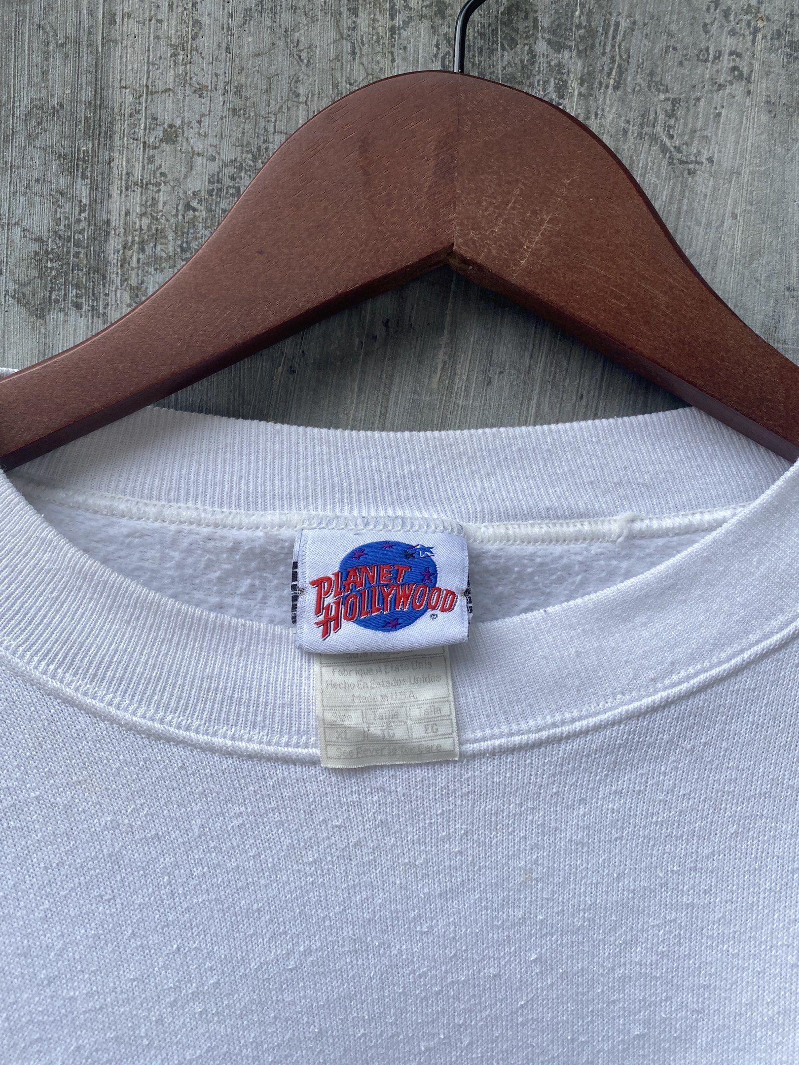 Planet Hollywood Beverly Hills Sweatshirt (Category: Coats, Jackets and Outerwear) located in San Pablo. Submitted by johnalmend72681 (Listing ID 1421342585, Image 2). Description: - White Planet Hollywood Beverly Hills sweatshirt - Features a small logo on the front - Large graphic on the back with a car and palm trees - Long sleeves - Crew neck - Made of soft material - Tag is visible.