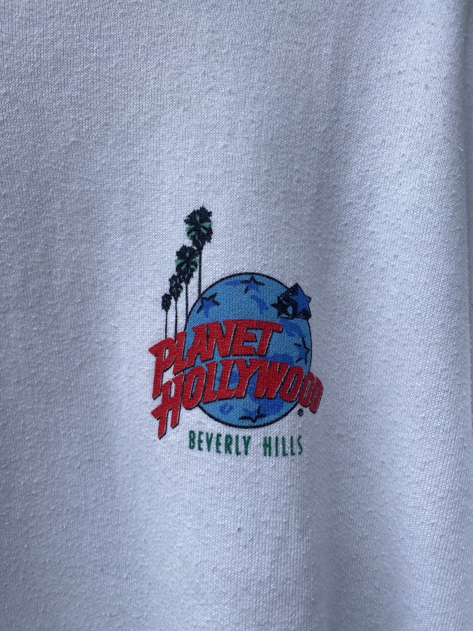 Planet Hollywood Beverly Hills Sweatshirt (Category: Coats, Jackets and Outerwear) located in San Pablo. Submitted by johnalmend72681 (Listing ID 1421342585, Image 3). Description: - White Planet Hollywood Beverly Hills sweatshirt - Features a small logo on the front - Large graphic on the back with a car and palm trees - Long sleeves - Crew neck - Made of soft material - Tag is visible.