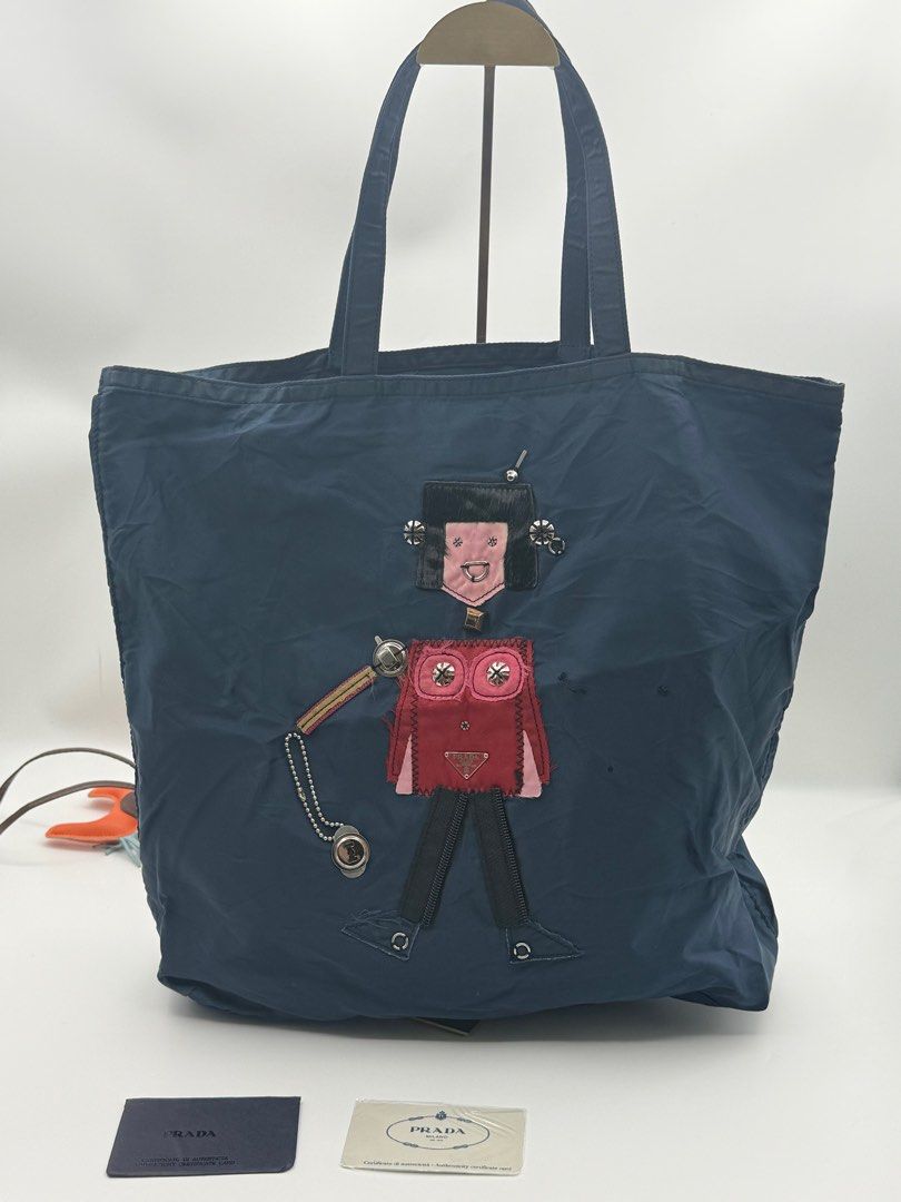 Prada Robot Tote Bag (Category: Luxury Bags & Wallets) located in Caloocan City. Submitted by rossvault2 (Listing ID 1421324161, Image 3). Description: - Prada tote bag - Navy blue color - Unique robot design on the front - Zipper closure - Interior pocket - Double handles - Prada logo visible - Includes cards - lampo zip - please check photo for issue.
