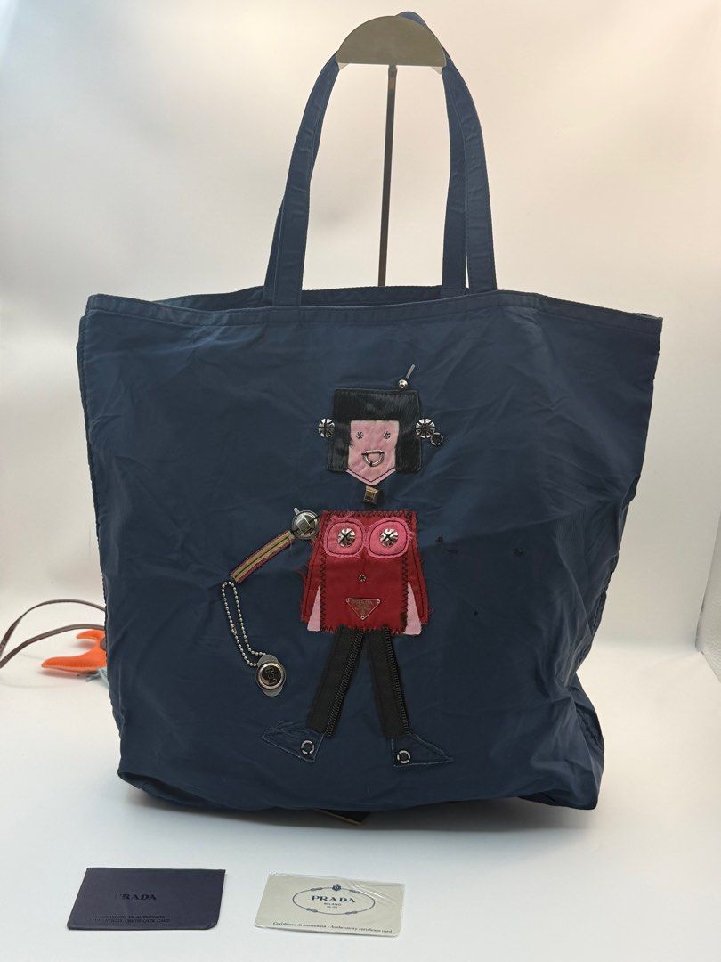 Prada Robot Tote Bag (Category: Luxury Bags & Wallets) located in Caloocan City. Submitted by rossvault2 (Listing ID 1421324161, Image 1). Description: - Prada tote bag - Navy blue color - Unique robot design on the front - Zipper closure - Interior pocket - Double handles - Prada logo visible - Includes cards - lampo zip - please check photo for issue.