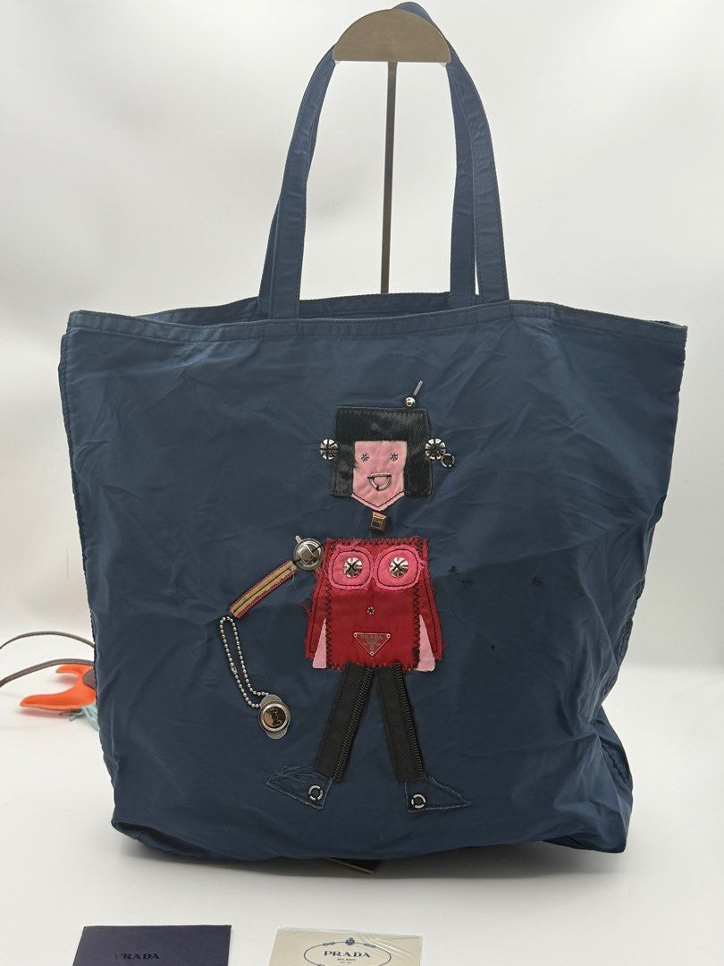 Prada Robot Tote Bag (Category: Luxury Bags & Wallets) located in Caloocan City. Submitted by rossvault2 (Listing ID 1421324161, Image 2). Description: - Prada tote bag - Navy blue color - Unique robot design on the front - Zipper closure - Interior pocket - Double handles - Prada logo visible - Includes cards - lampo zip - please check photo for issue.