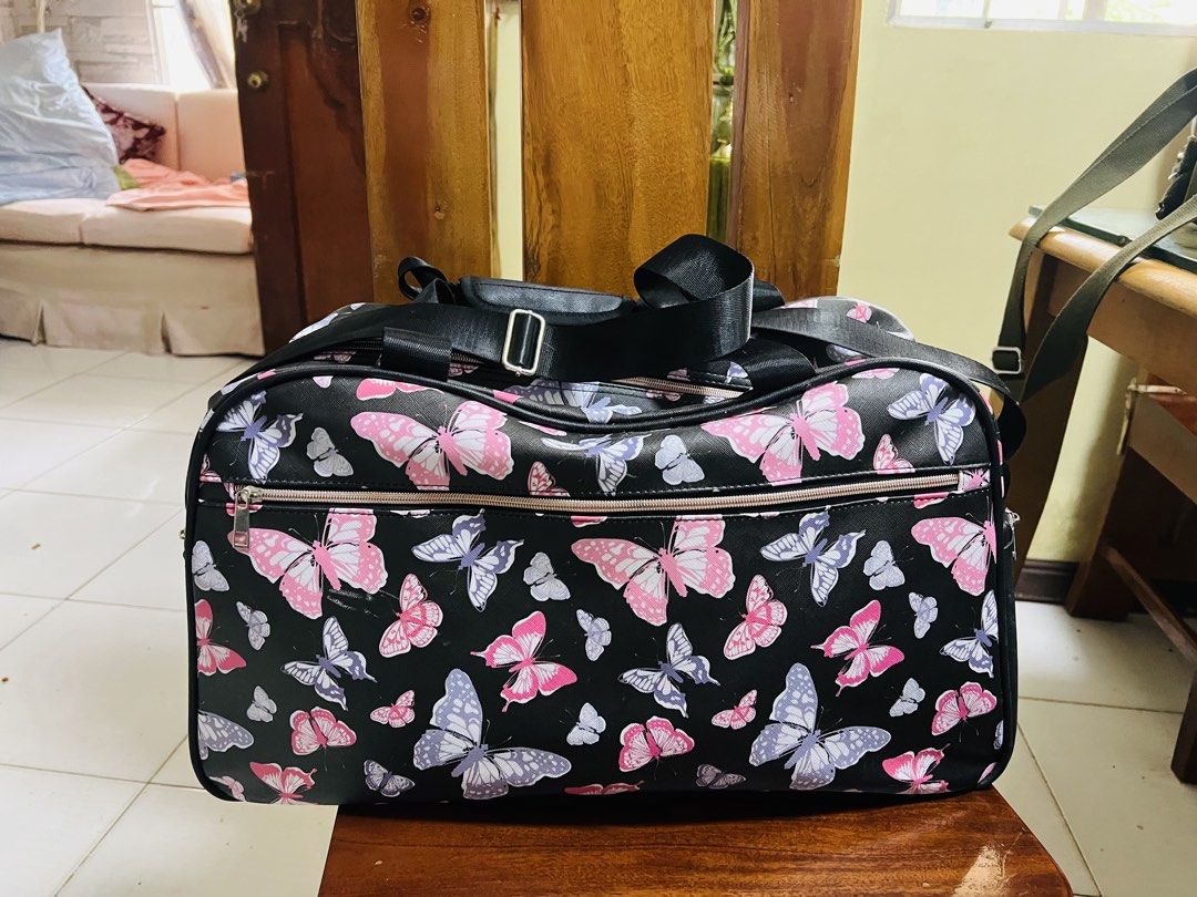 Butterfly Print Duffle Bag (Category: Luxury Bags & Wallets) located in Antipolo. Submitted by murapod2 (Listing ID 1421617007, Image 1). Description: Duffle bag features a vibrant butterfly print on a black background. It has a top handle and a detachable shoulder strap for versatile carrying options. The bag includes a main compartment and a side pocket, both with zipper closures. The interior is lined with black fabric. Came from Hawaii .