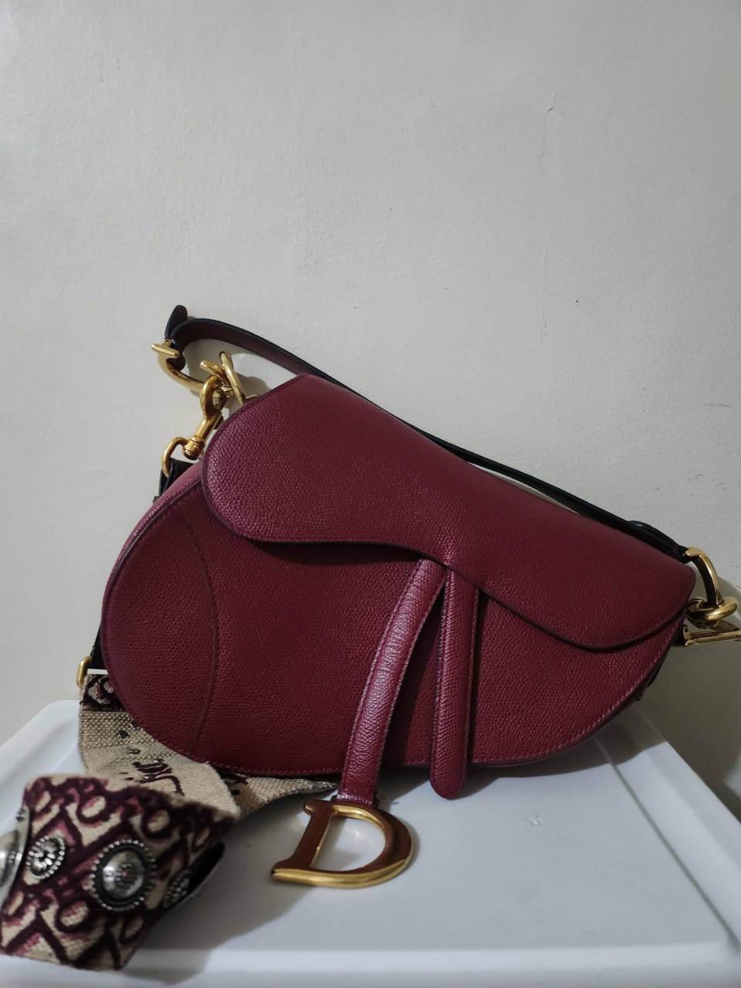 Dior Mini Saddle Bag Burgundy (Category: Luxury Bags & Wallets) located in Quezon City. Submitted by preloved4ever_ (Listing ID 1421462788, Image 1). Description: - Authentic Dior Saddle Bag in Burgundy - Gold-tone hardware - Detachable shoulder strap with Christian Dior logo - Iconic saddle shape with 'D' charm - Patterned strap design with silver-tone embellishments - Crafted from leather Condition: 9/10 Rfs: downsizing collection.