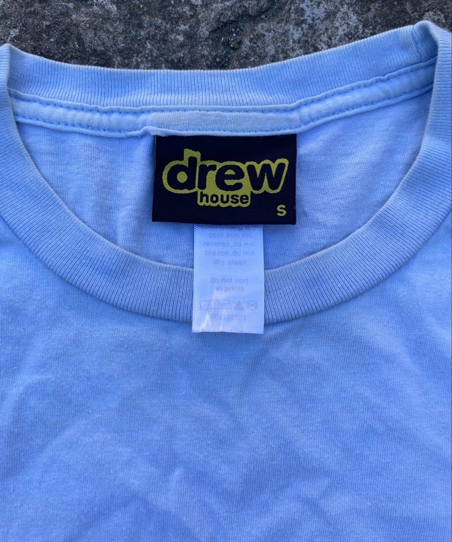 Drew House Smiley Face T-shirt (Category: Tshirts & Polo Shirts ) located in Bacolod City. Submitted by 0411a (Listing ID 1421558276, Image 2). Description: Light blue Drew House T-shirt featuring a yellow smiley face with the brand name "drew" in black. The shirt has a small size tag. The tag also indicates the brand name "drew house"..