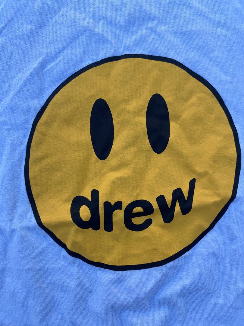 Drew House Smiley Face T-shirt (Category: Tshirts & Polo Shirts ) located in Bacolod City. Submitted by 0411a (Listing ID 1421558276, Image 3). Description: Light blue Drew House T-shirt featuring a yellow smiley face with the brand name "drew" in black. The shirt has a small size tag. The tag also indicates the brand name "drew house"..