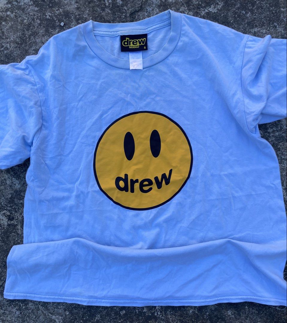 Drew House Smiley Face T-shirt (Category: Tshirts & Polo Shirts ) located in Bacolod City. Submitted by 0411a (Listing ID 1421558276, Image 1). Description: Light blue Drew House T-shirt featuring a yellow smiley face with the brand name "drew" in black. The shirt has a small size tag. The tag also indicates the brand name "drew house"..