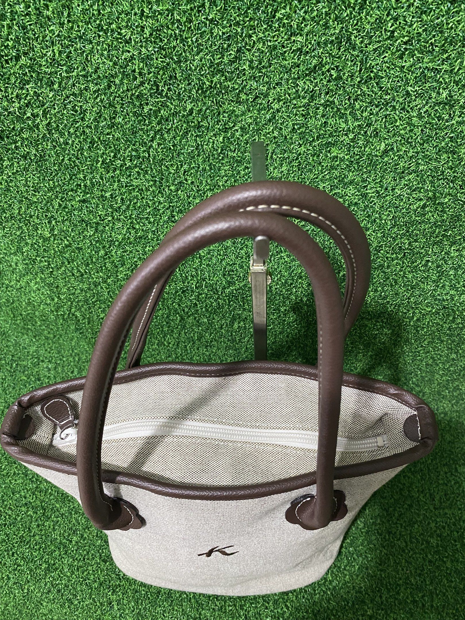 Kitamura Tote Bag (Category: Tote Bags) located in Naga. Submitted by taurusg (Listing ID 1421559546, Image 3). Description: - Kitamura tote bag - Light-colored exterior - Brown leather handles and trim - Pink fabric interior - Interior zippered pocket - Top zipper closure - Small logo on front - Oval-shaped bottom.