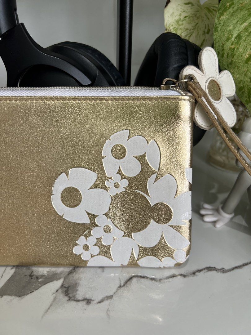Marc Jacobs Daisy Gold Pouch (Category: Luxury Bags & Wallets) located in Cavite. Submitted by slumbermanila (Listing ID 1421555543, Image 3). Description: with stained in lining part Gold pouch with white daisy flower design. Features a wrist strap and a zipper closure. The interior lining has some stains. The pouch is approximately 9 inches long and 6 inches wide. This is a pre-loved item sourced from thrift finds. Kindly manage expectations, a