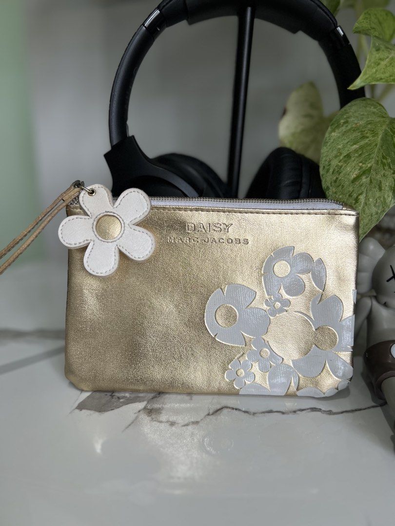 Marc Jacobs Daisy Gold Pouch (Category: Luxury Bags & Wallets) located in Cavite. Submitted by slumbermanila (Listing ID 1421555543, Image 1). Description: with stained in lining part Gold pouch with white daisy flower design. Features a wrist strap and a zipper closure. The interior lining has some stains. The pouch is approximately 9 inches long and 6 inches wide. This is a pre-loved item sourced from thrift finds. Kindly manage expectations, a