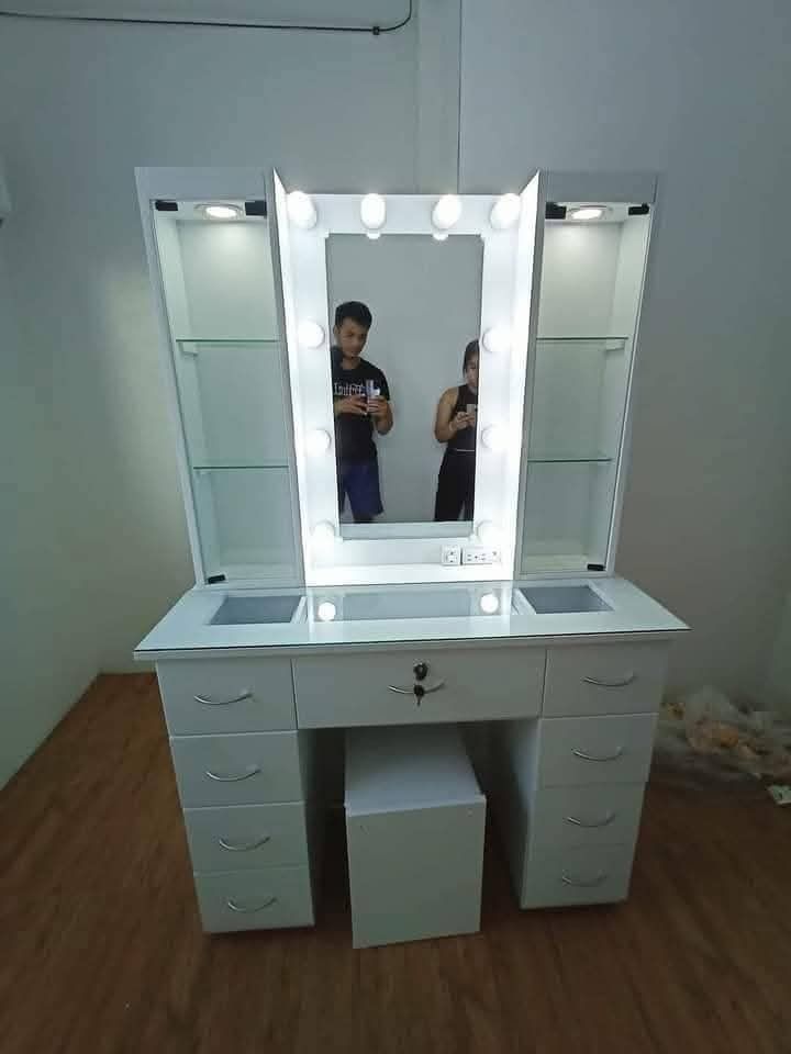Vanity Table with Mirror and Lights (Category: Tables & Sets) located in Mabalacat. Submitted by arlenemamangun01 (Listing ID 1421568325, Image 1). Description: - White vanity table with large mirror and built-in lights - Multiple drawers and side cabinets with glass shelves - Includes matching stool - Sleek design - Ample storage space - Ideal for makeup and beauty routines.