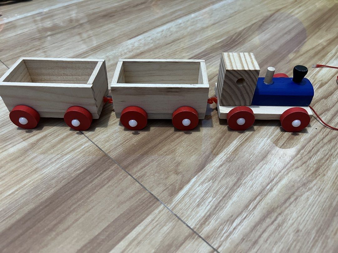 Wooden Toy Train Set (Category: Kids Toys) located in Bacoor. Submitted by momofkas1 (Listing ID 1421515850, Image 1). Description: - Wooden toy train set - Features a blue engine and two cargo cars - Red wheels with white centers - Made of natural wood - Painted with red and blue accents - Connected by red strings - Classic toy for imaginative play.