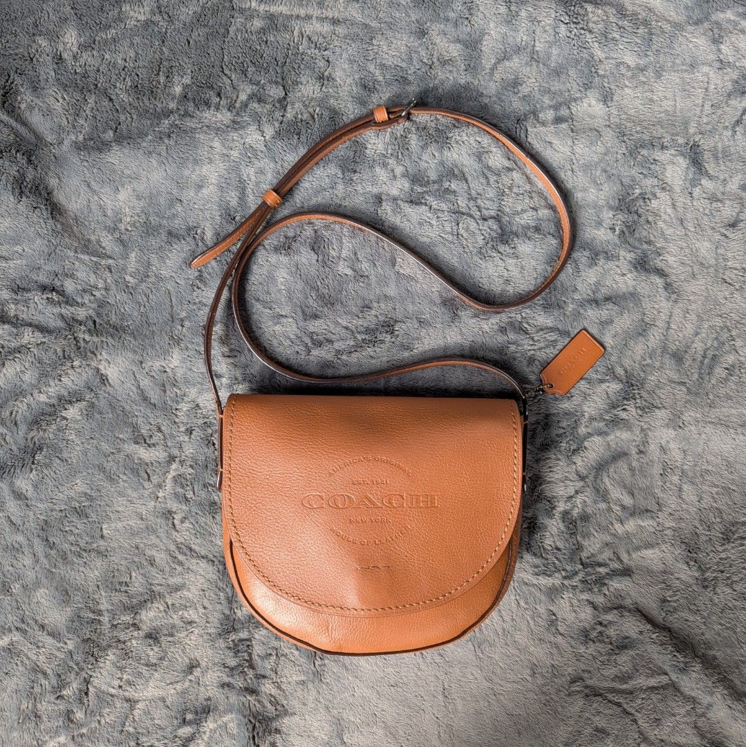 Coach Saddle Crossbody Bag (Category: Luxury Bags & Wallets) located in Manila. Submitted by eladp (Listing ID 1421730035, Image 1). Description: - Authentic Coach crossbody bag -Preloved RETAIL item - Saddle bag design - Tan leather exterior - Adjustable strap - Magnetic snap closure - Includes Coach hangtag - Interior zippered pocket - Additional slip pocket.