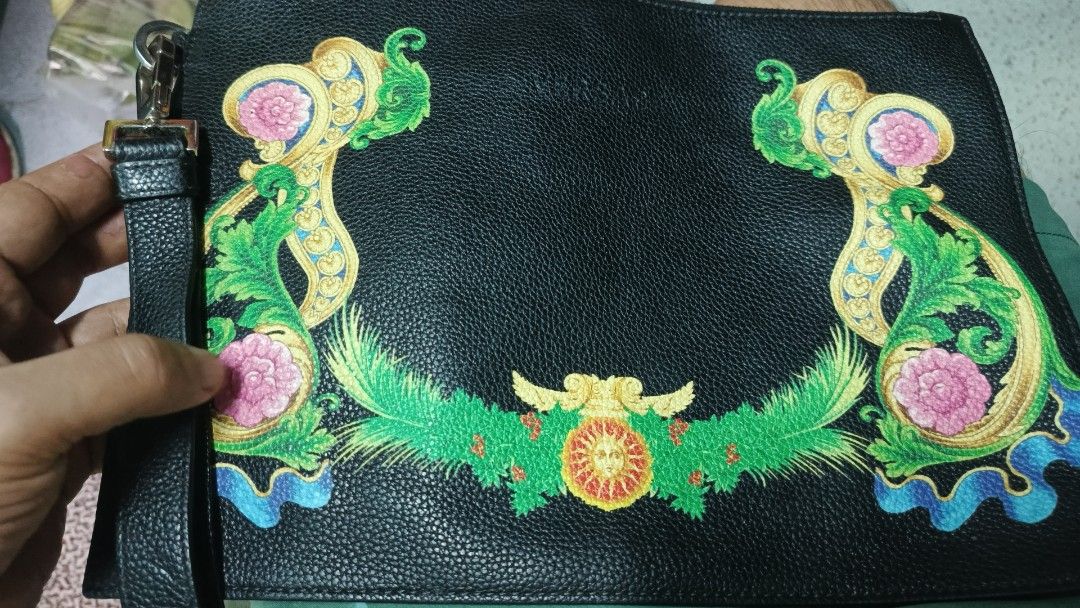 Versace Clutch Bag with Floral Design (Category: Luxury Bags & Wallets) located in Makati City. Submitted by macdwyneki84361 (Listing ID 1421650865, Image 1). Description: - Versace clutch bag - Black exterior - Wrist strap - Silver-tone clasp with Versace logo engraving - Interior leather patch with brand logo - Features vibrant floral design in green, pink, and gold.