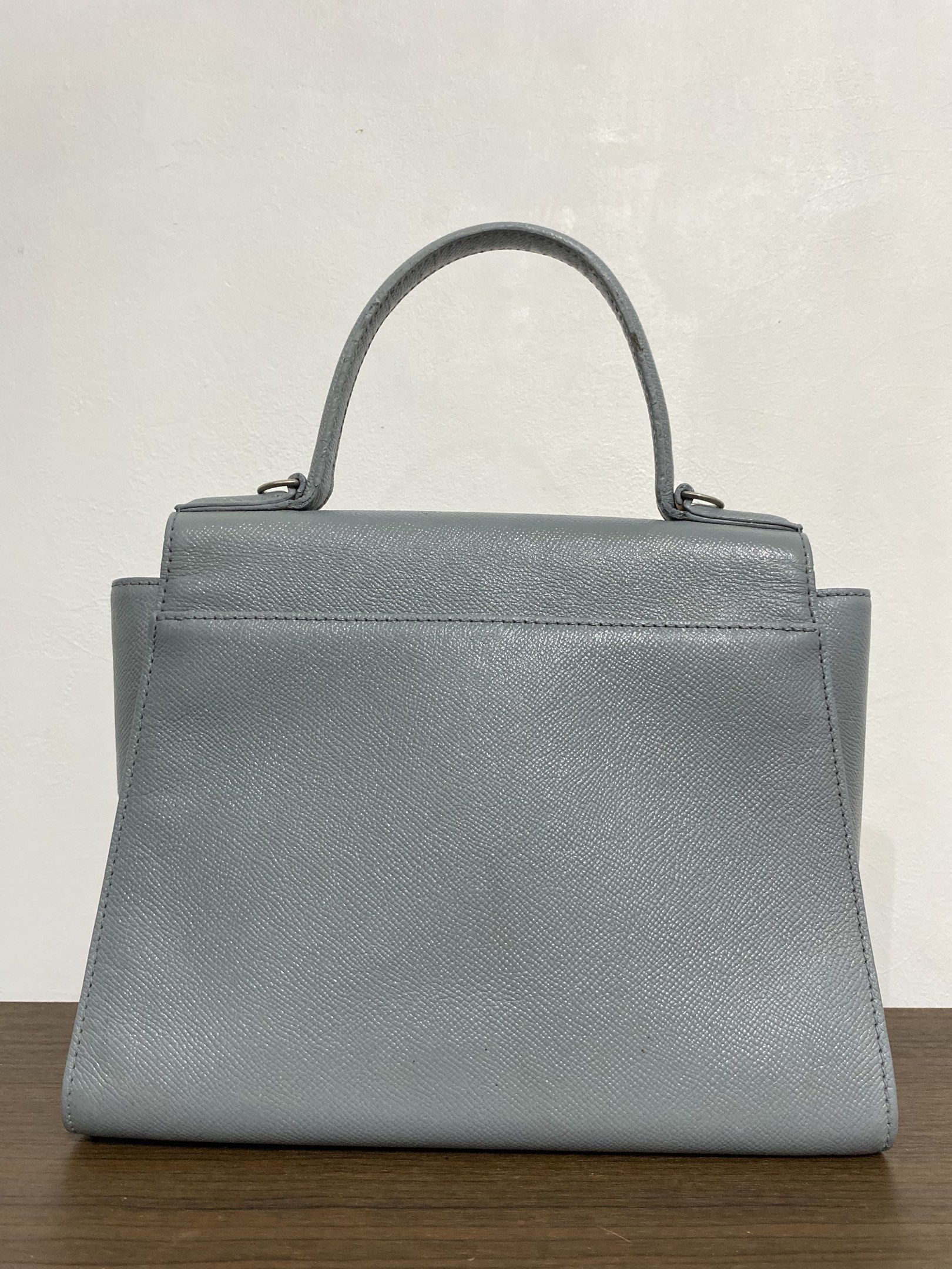 Couronne Handbag (Category: Luxury Bags & Wallets) located in Bulacan. Submitted by knklittlecloset (Listing ID 1421803343, Image 2). Description: Couronne handbag features a structured design with a top handle and a flap closure. It has a silver-tone metal detail on the front and a detachable shoulder strap. The interior includes a zippered pocket. The bag is in a light blue color. The bottom of the bag has four metal feet. Detachable strap and 