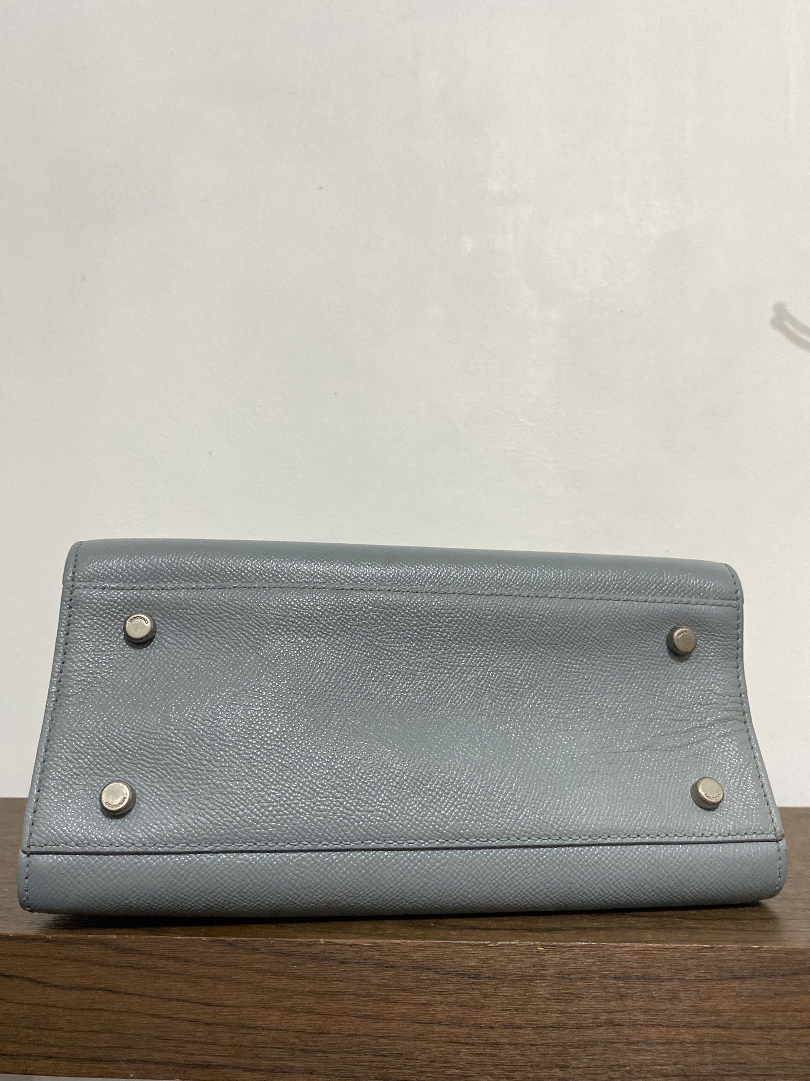 Couronne Handbag (Category: Luxury Bags & Wallets) located in Bulacan. Submitted by knklittlecloset (Listing ID 1421803343, Image 3). Description: Couronne handbag features a structured design with a top handle and a flap closure. It has a silver-tone metal detail on the front and a detachable shoulder strap. The interior includes a zippered pocket. The bag is in a light blue color. The bottom of the bag has four metal feet. Detachable strap and 