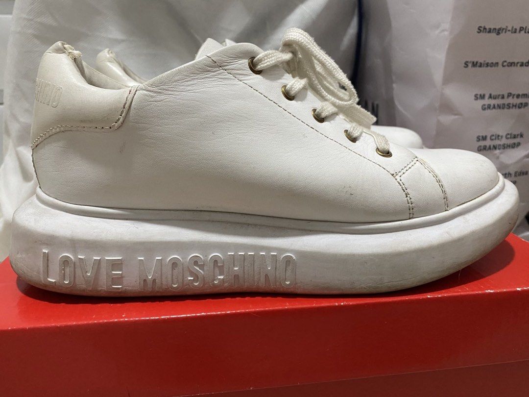 Love Moschino White Sneakers Size 38 (Category: Sneakers) located in Mandaluyong City. Submitted by getbounced (Listing ID 1421896849, Image 3). Description: White Love Moschino sneakers with heart details. Features a thick sole with "LOVE MOSCHINO" printed on the side. The size is 38. Includes the original box and a dust bag. The soles have heart-shaped patterns. The insole has "LOVE MOSCHINO" printed all over it..