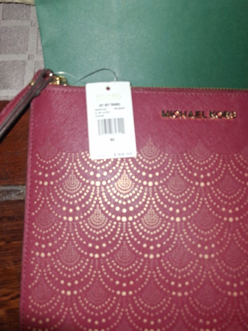 Michael Korrs Jet Set Travel Clutch (Category: Luxury Bags & Wallets) located in Quezon City. Submitted by cncarousel (Listing ID 1421891893, Image 3). Description: Authentic Michael Kors Jet Set Travel clutch. Features a burgundy color with a decorative pattern on the front. Includes a wrist strap and a zipper closure. Comes with a Michael Kors tag and a green shopping bag. The tag indicates the color is 'Mulberry'..