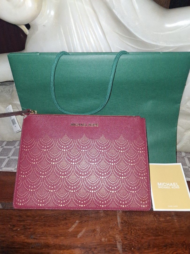 Michael Korrs Jet Set Travel Clutch (Category: Luxury Bags & Wallets) located in Quezon City. Submitted by cncarousel (Listing ID 1421891893, Image 1). Description: Authentic Michael Kors Jet Set Travel clutch. Features a burgundy color with a decorative pattern on the front. Includes a wrist strap and a zipper closure. Comes with a Michael Kors tag and a green shopping bag. The tag indicates the color is 'Mulberry'..
