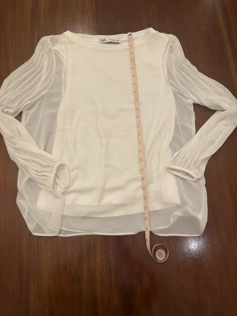 Zara White Blouse with Sheer Sleeves (Category: Blouses) located in Mandaue City. Submitted by marginiz (Listing ID 1421891302, Image 3). Description: White blouse from Zara with sheer sleeves. Features a round neckline and long sleeves with pleated details. The blouse has a layered design with a solid white inner layer. Measurements are approximately 22 inches in length and 20 inches across the chest. Size is XS..