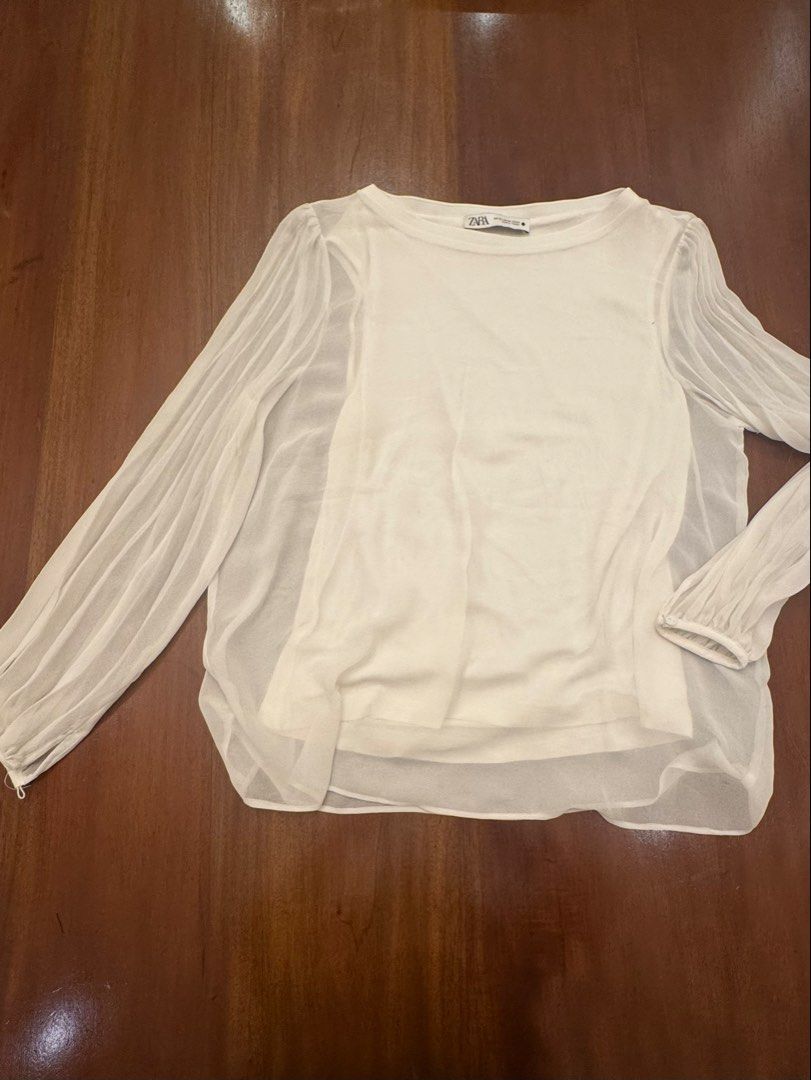 Zara White Blouse with Sheer Sleeves (Category: Blouses) located in Mandaue City. Submitted by marginiz (Listing ID 1421891302, Image 1). Description: White blouse from Zara with sheer sleeves. Features a round neckline and long sleeves with pleated details. The blouse has a layered design with a solid white inner layer. Measurements are approximately 22 inches in length and 20 inches across the chest. Size is XS..