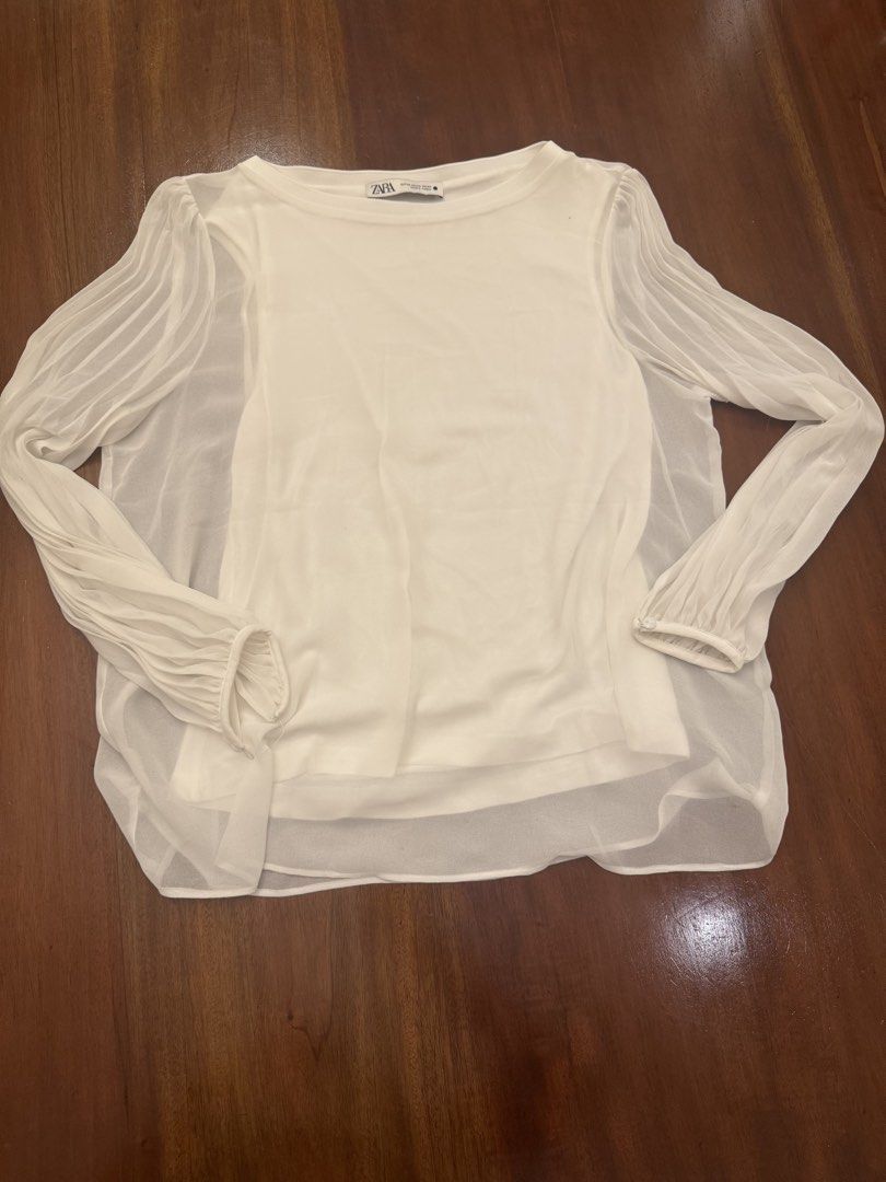 Zara White Blouse with Sheer Sleeves (Category: Blouses) located in Mandaue City. Submitted by marginiz (Listing ID 1421891302, Image 2). Description: White blouse from Zara with sheer sleeves. Features a round neckline and long sleeves with pleated details. The blouse has a layered design with a solid white inner layer. Measurements are approximately 22 inches in length and 20 inches across the chest. Size is XS..